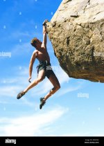 a-rock-climber-hanging-on-to-a-rock-with-one-hand-2D9CXX4.jpg